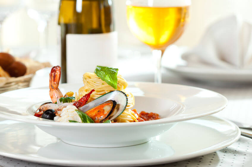 Spaghetti allo scoglio con un bicchiere di Verdicchio di Jesi sullo sfondo